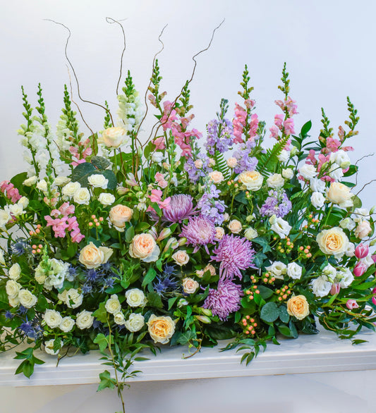 An assortment of flowers and greens arranged in a low horizontal fashion to look like a growing garden