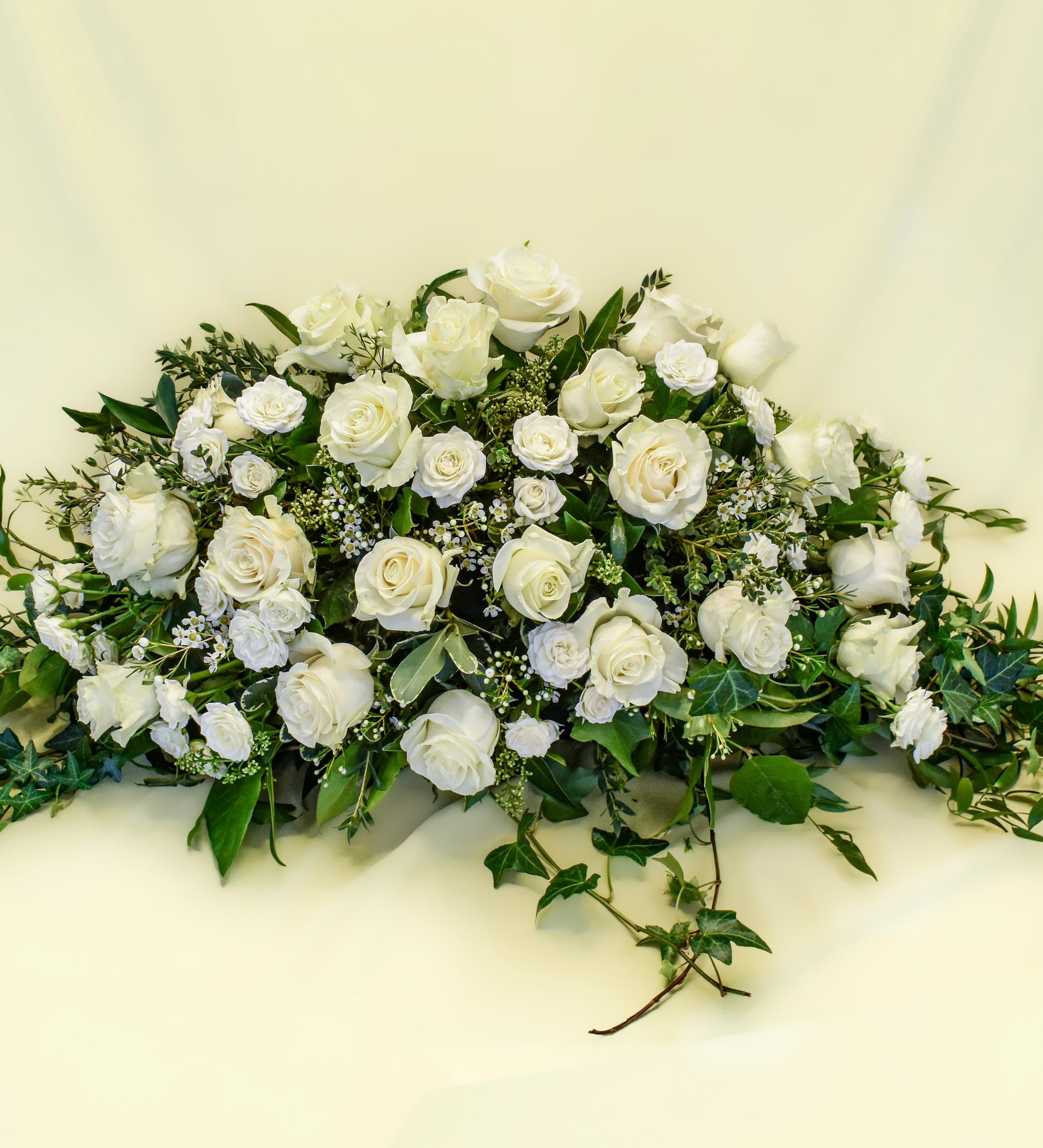 White roses and spray roses arranged with white wax flower and greens in a casket spray