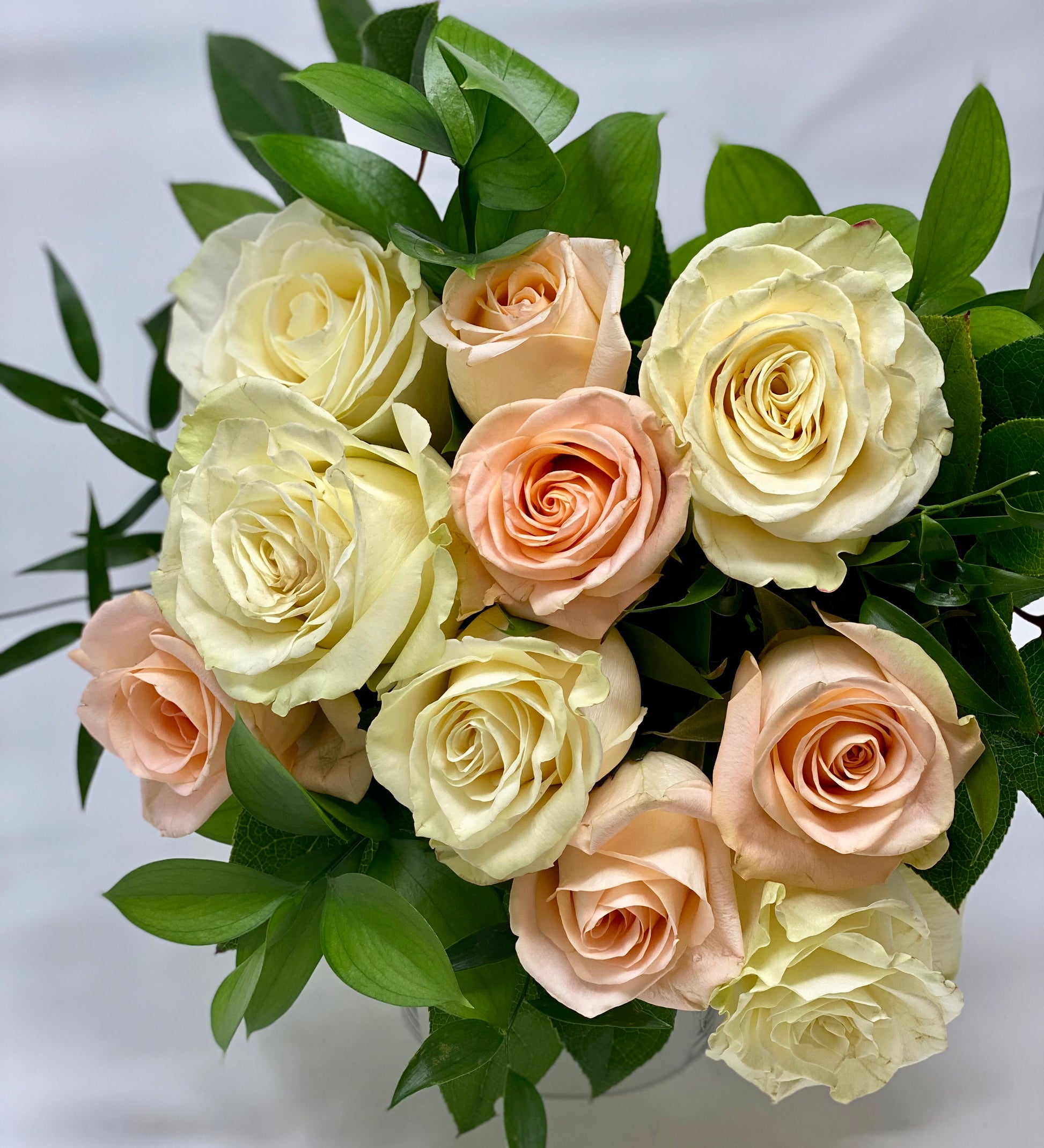 Peach and cream coloured roses arranged with greens in a bouquet