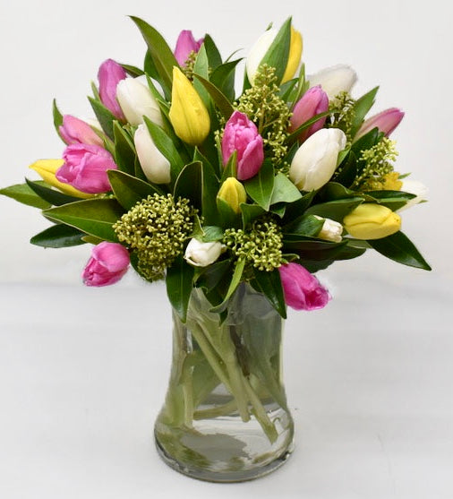 Pastel coloured tulips with greens in a tall vase